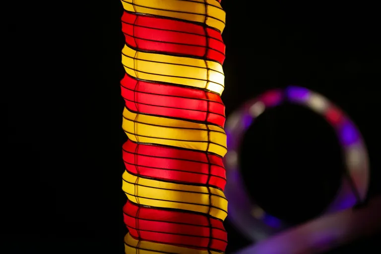 A colorful lamp with vertical red and yellow stripes, radiating light against a dark background, suggesting a warm and inviting atmosphere suitable for both indoor and outdoor settings.