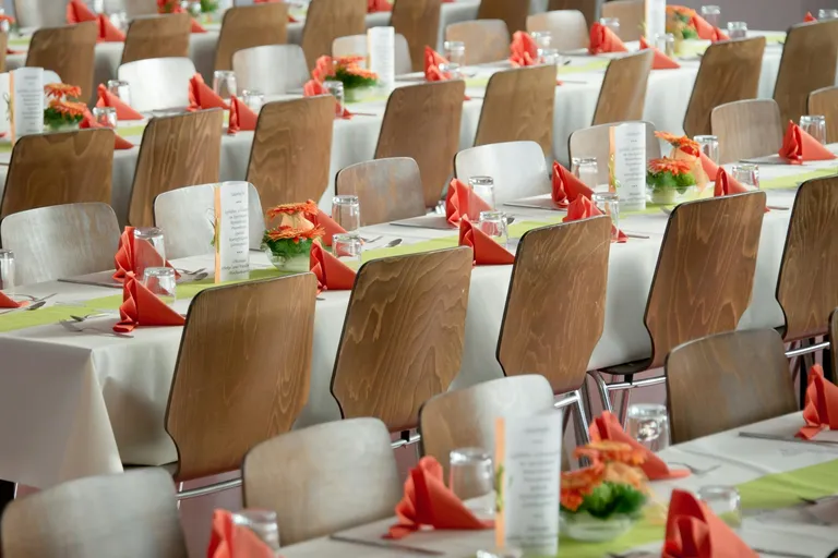 A beautifully arranged dining hall with wooden chairs and tables set for an event, featuring pink napkins and floral centerpieces.