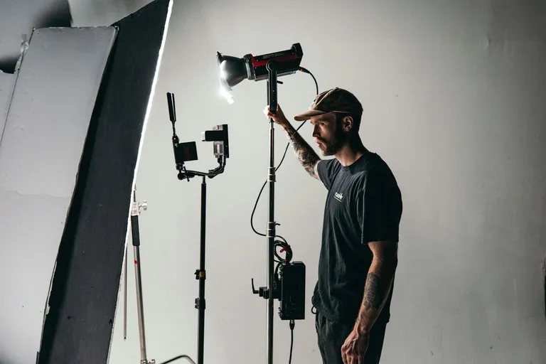A man adjusting a studio light on a stand inside a photography studio, demonstrating event lighting design equipment.