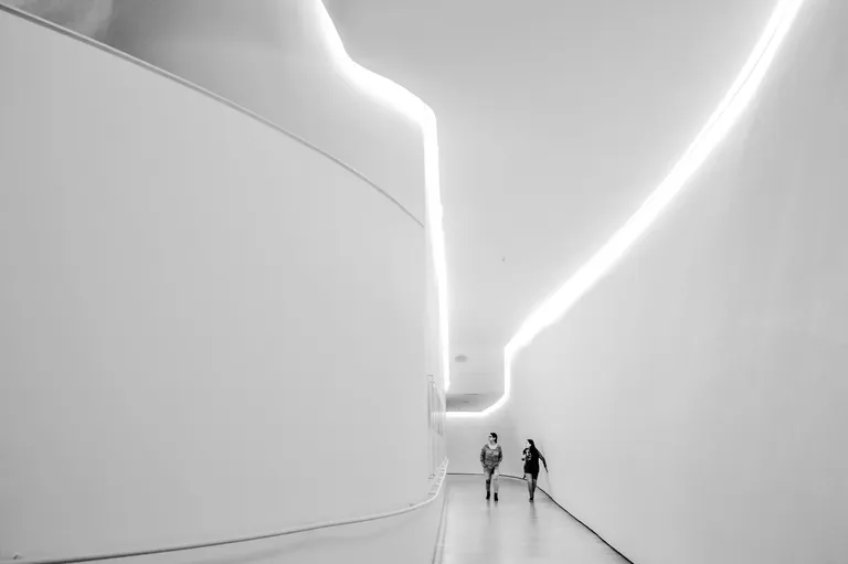 A modern, minimalist interior hallway with smooth white walls and soft lighting illuminating the curved architectural lines.