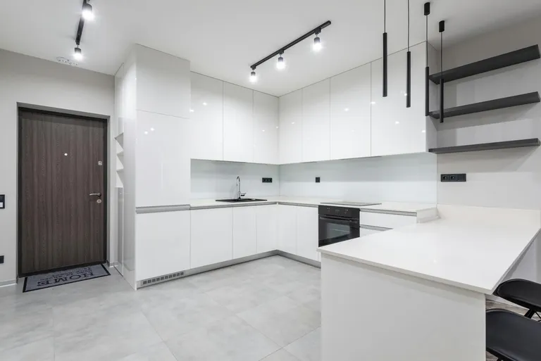 A modern kitchen design featuring glossy white cabinets, stainless steel appliances, and a minimalist aesthetic, highlighting the use of architectural lighting.