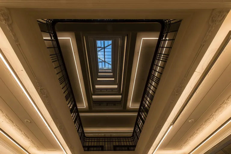 An overhead view of a multi-level architectural space featuring a skylight, elegant railings, and a pattern of modern interior design elements that emphasizes lighting and structure.