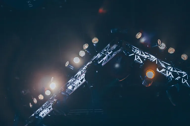 A view of stage lighting equipment with lights positioned on a truss, illuminating the scene with a mix of colors and brightness.