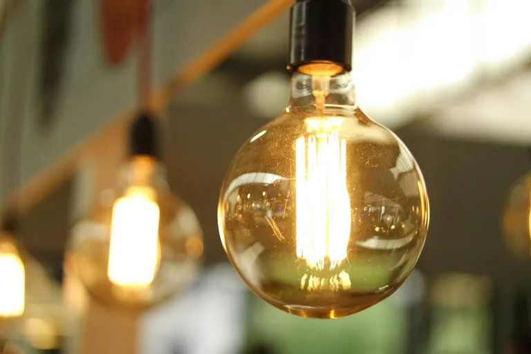 A close-up of a vintage-style light bulb glowing warmly, reflecting its surroundings, symbolizing artistic lighting design.